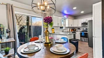 A modern kitchen with white cabinets, a stainless steel refrigerator, and a dining area with a round table set for two.