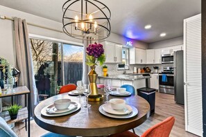 A modern kitchen with white cabinets, a stainless steel refrigerator, and a dining area with a round table set for two.