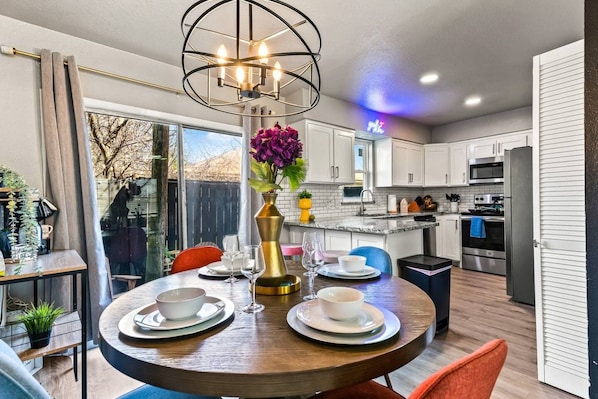 A modern kitchen with white cabinets, a stainless steel refrigerator, and a dining area with a round table set for two.