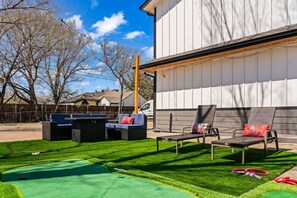 A backyard with a green lawn, outdoor seating, and a white building.