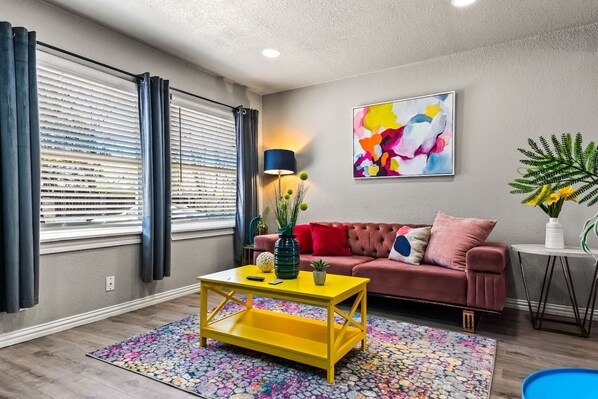 A living room with a sofa, a yellow coffee table, and a painting on the wall.