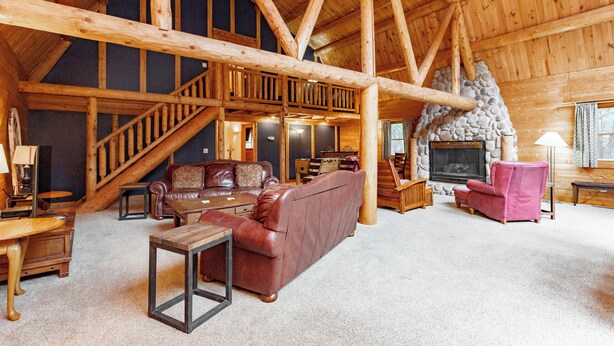 A spacious loft-style living area with a high ceiling, wooden beams, a fireplace, and a staircase leading to an upper level. - Family & Dog Friendly Escape w/ 2 Hot Tubs (McHenry)