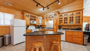 A wooden cabin-style kitchen with a central island, wooden stools, and built-in appliances. - Family & Dog Friendly Escape w/ 2 Hot Tubs (McHenry)