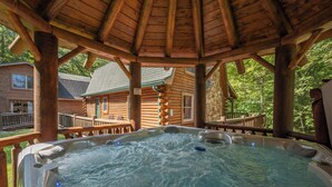 A hot tub area with a wooden gazebo structure, surrounded by a wooden deck and a stone wall. - Family & Dog Friendly Escape w/ 2 Hot Tubs (McHenry)
