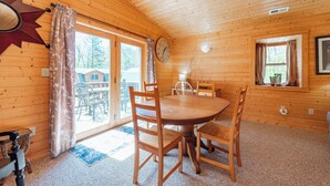 Une cabane en bois avec une table à manger ronde et des chaises, une grande fenêtre avec des rideaux et une décoration en forme d’étoile sur le mur.