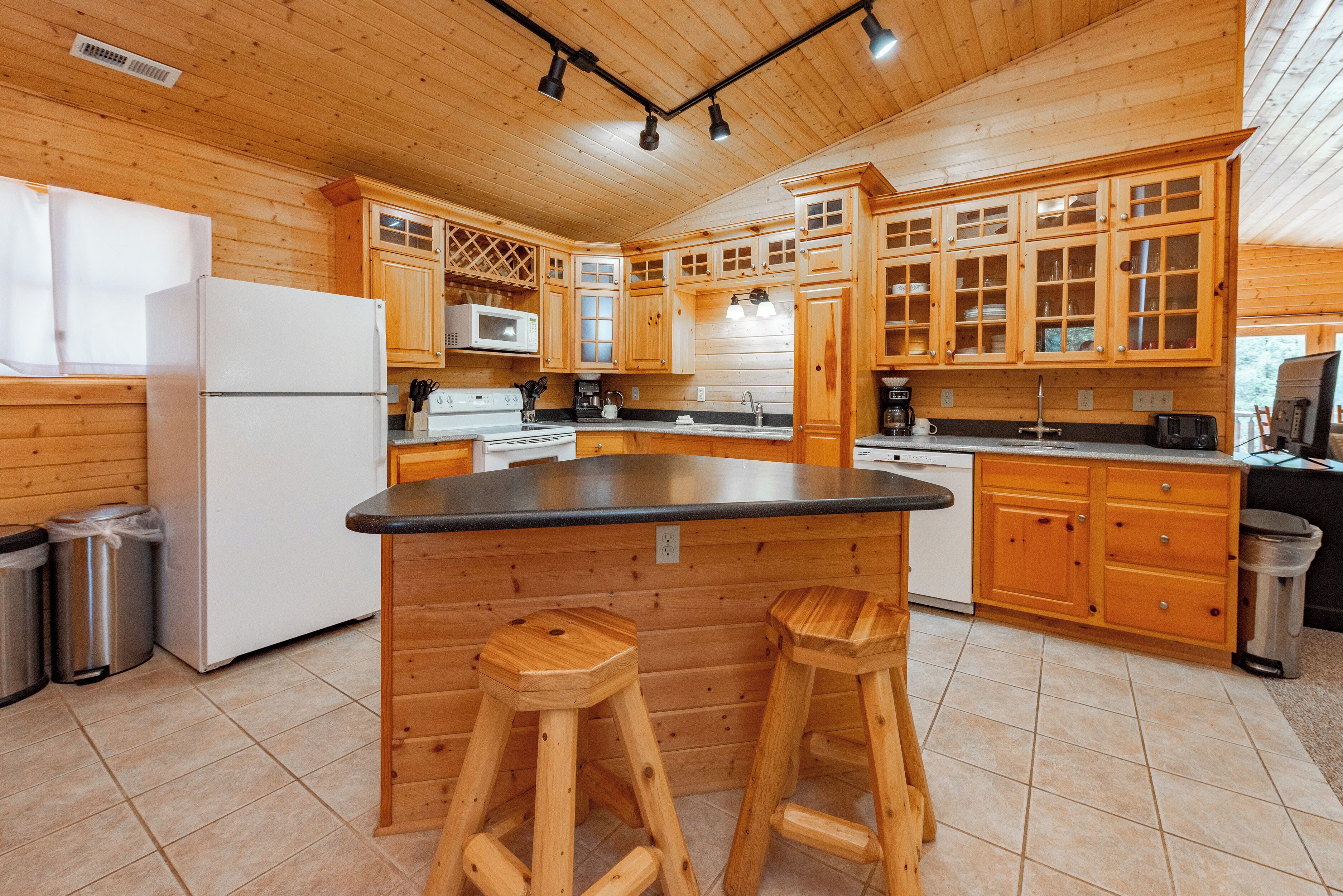 A wooden cabin-style kitchen with a central island, wooden stools, and built-in appliances.