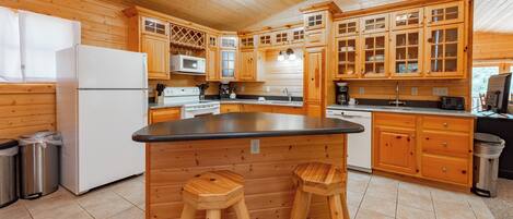 A wooden cabin-style kitchen with a central island, wooden stools, and built-in appliances.