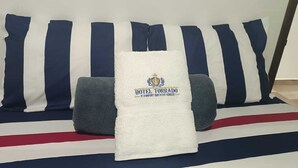 A bed with a white blanket and pillows, a striped pillowcase, and a flag design on the bedspread.
