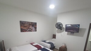 A hotel room with two single beds, a wall-mounted TV, a ceiling fan, and a poster of San Francisco.
