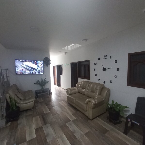 A living room with a beige leather sofa, a television mounted on the wall, and a clock. - Hotel Torrado (Ocaña)