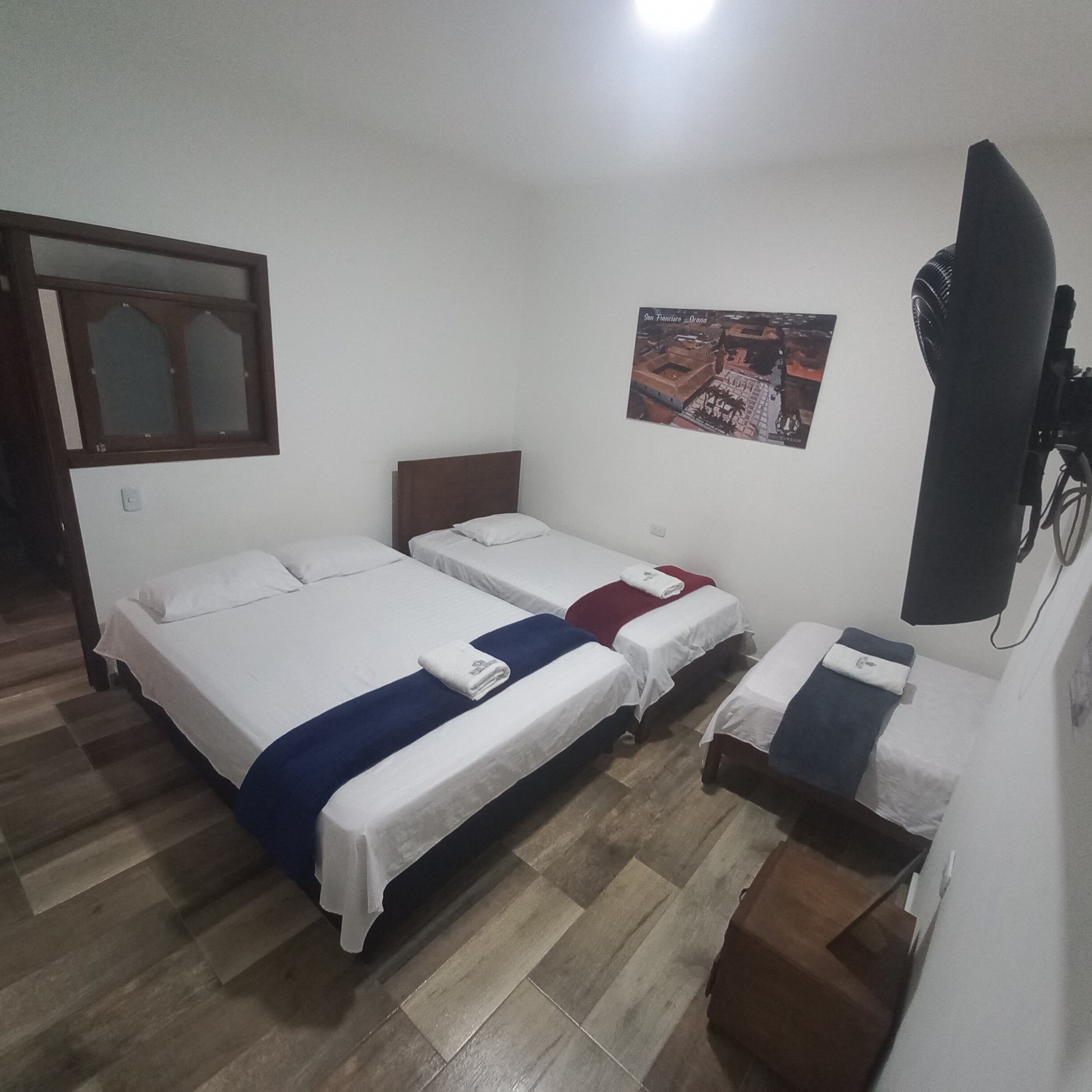 Una habitación con dos camas, suelo de madera, un televisor montado en la pared y un póster.