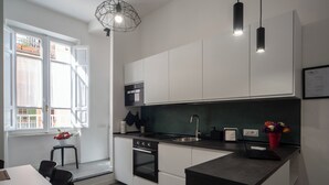 A modern kitchen with white cabinets, a black countertop, a built-in oven, a sink, and pendant lighting.