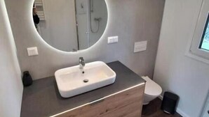 A modern bathroom with a round mirror, a white sink, and a wooden vanity.
