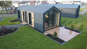 A modern building with a sloped roof, large windows, and a paved patio area. - Holiday Home 2 (Sohren)
