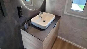 A bathroom with a modern design, featuring a round mirror, a white sink, and a wooden vanity. - Holiday Home 2 (Sohren)
