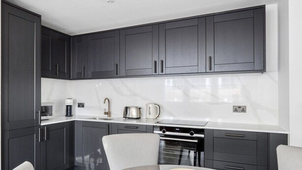 A modern kitchen with dark cabinets, a white countertop, and a round dining table with chairs. - Impeccable 2-bed Apartment in London (London)