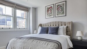 A bedroom with a large bed, two bedside tables, a window with curtains, and two abstract wall art pieces. - Impeccable 2-bed Apartment in London (London)