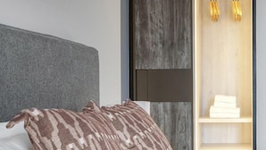 A modern hotel room with a grey headboard, a patterned throw pillow, and a built-in wardrobe with a wooden finish and hanging lights. - Charming 2 Bedrooms Apartment in London (London)