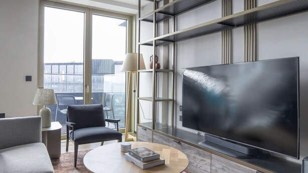 A modern living room with a large flat-screen TV, a sofa, a coffee table with books, and a floor lamp. - Charming 2 Bedrooms Apartment in London (London)