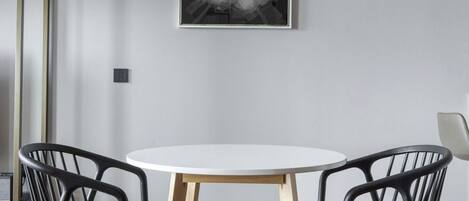 A room with a round table, two chairs, a framed abstract artwork on the wall, and a wooden floor.