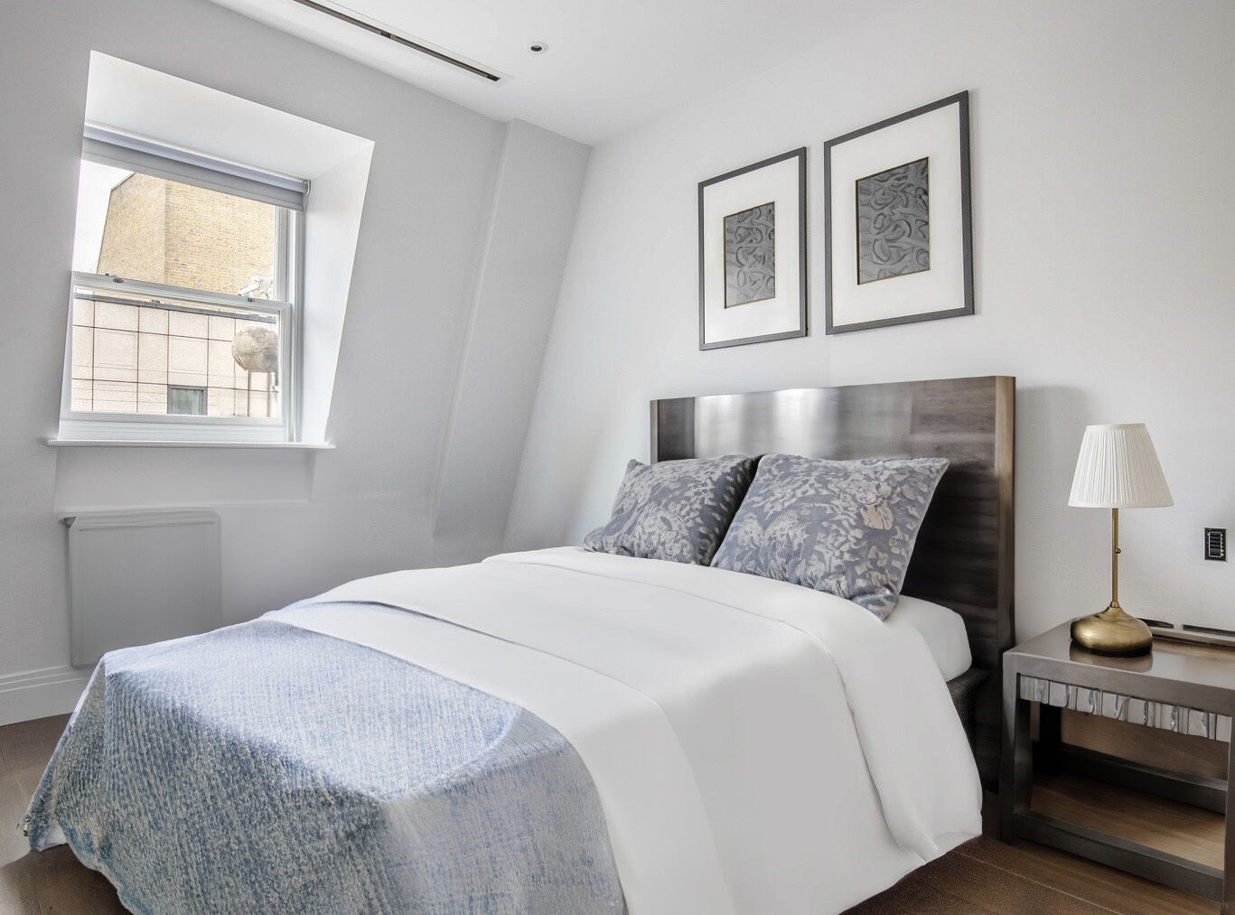 A modern bedroom with a large bed, a nightstand, a lamp, and two framed pictures on the wall.