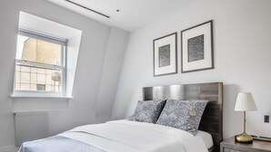 A modern bedroom with a large bed, a nightstand, a lamp, and two framed pictures on the wall. - Cozy 2 Bedrooms by Shoreditch (London)