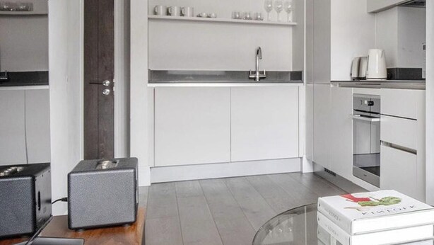 A modern kitchen with white cabinetry, a glass dining table, and a wooden countertop. - Cozy 2 Bedrooms by Shoreditch (London)