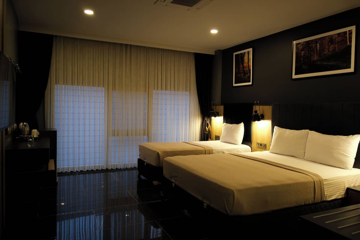 A hotel room with two beds, a large window with curtains, a flat-screen TV, and artwork on the walls.
