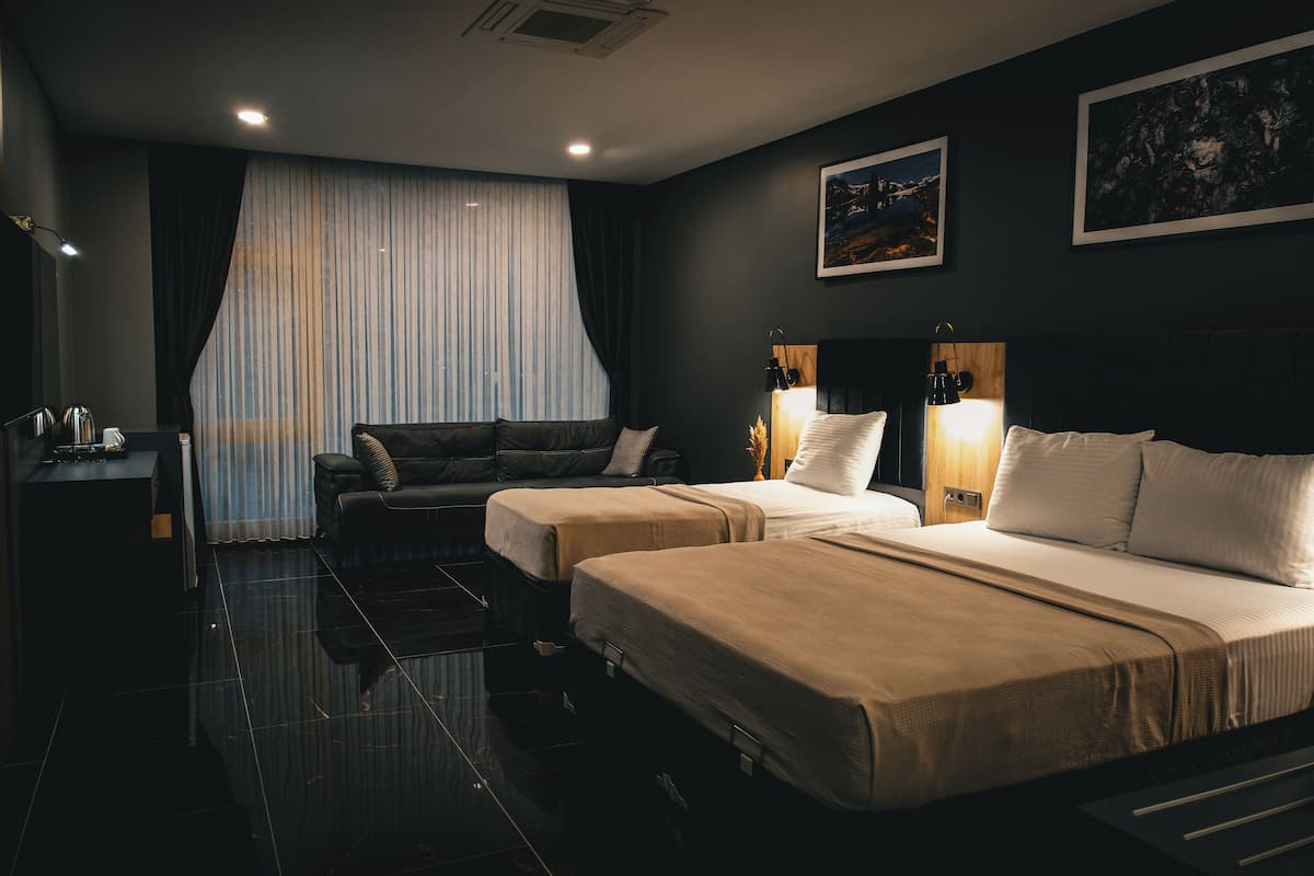 A hotel room with two beds, a desk, and a large window with curtains.