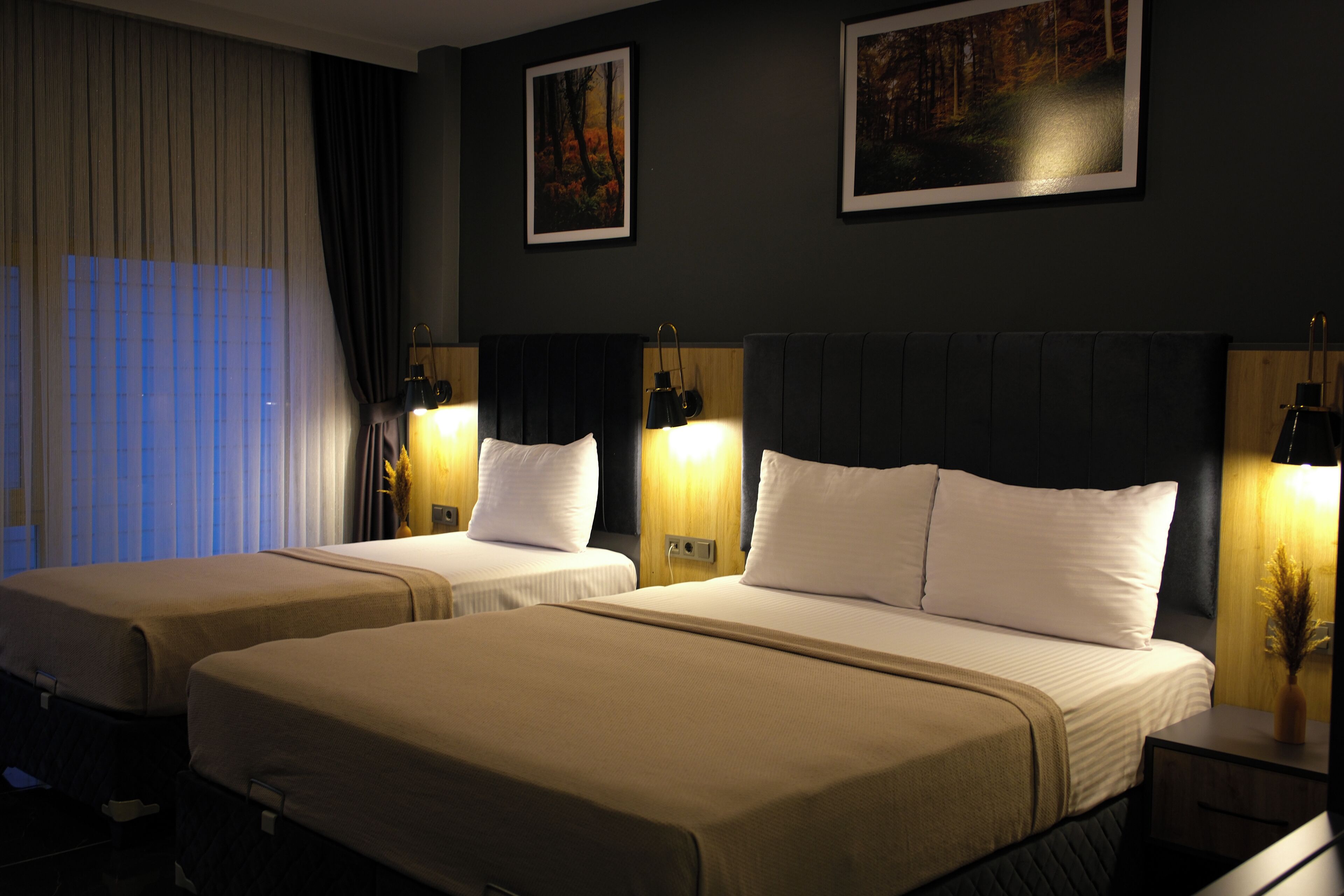 Une chambre d’hôtel avec deux lits, une grande fenêtre avec des stores et deux lampes fixées au mur.