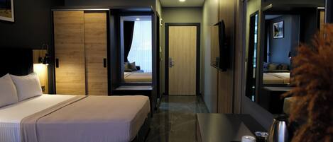 A modern hotel room with a large bed, a desk with a kettle, and a mirror.
