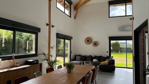 A spacious living area with a wooden dining table, a sofa, and a large window overlooking a garden.