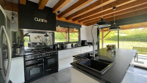 A modern kitchen with a black stove, white cabinets, and a large window overlooking greenery.