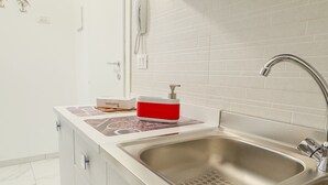A modern kitchen with a stainless steel sink, white cabinets, and a red soap dispenser on the countertop.