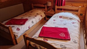 Une chambre confortable dans un chalet, avec deux lits en bois, chacun recouvert d’une couverture à motifs de cœurs rouges.