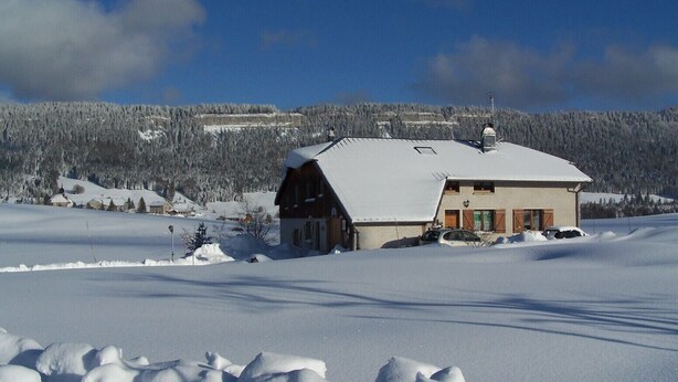 Un paysage enneigé avec un bâtiment en bois doté d’un toit en pente et d’une cheminée.