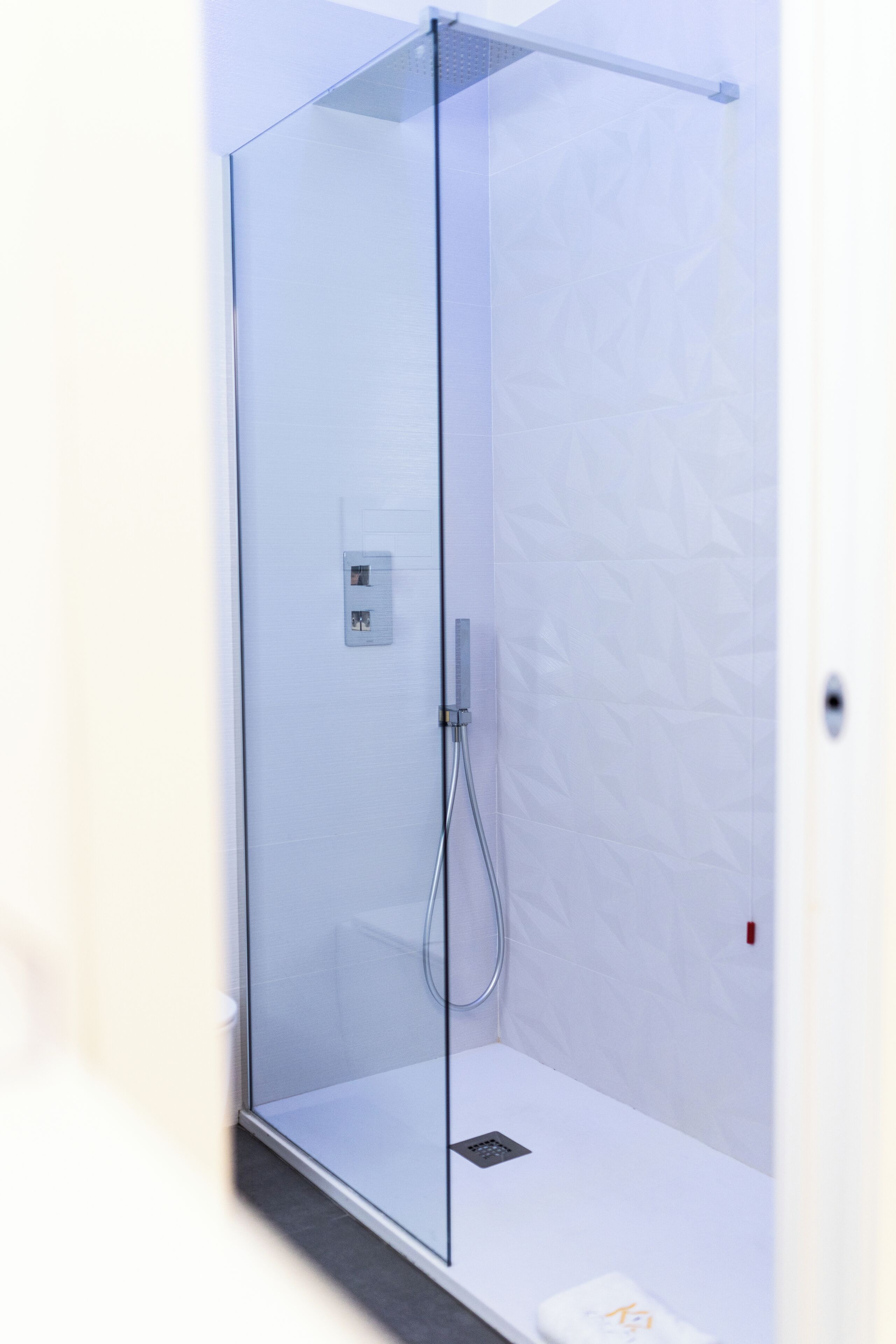 A modern shower enclosure with a glass door, a control panel, and a handheld showerhead.