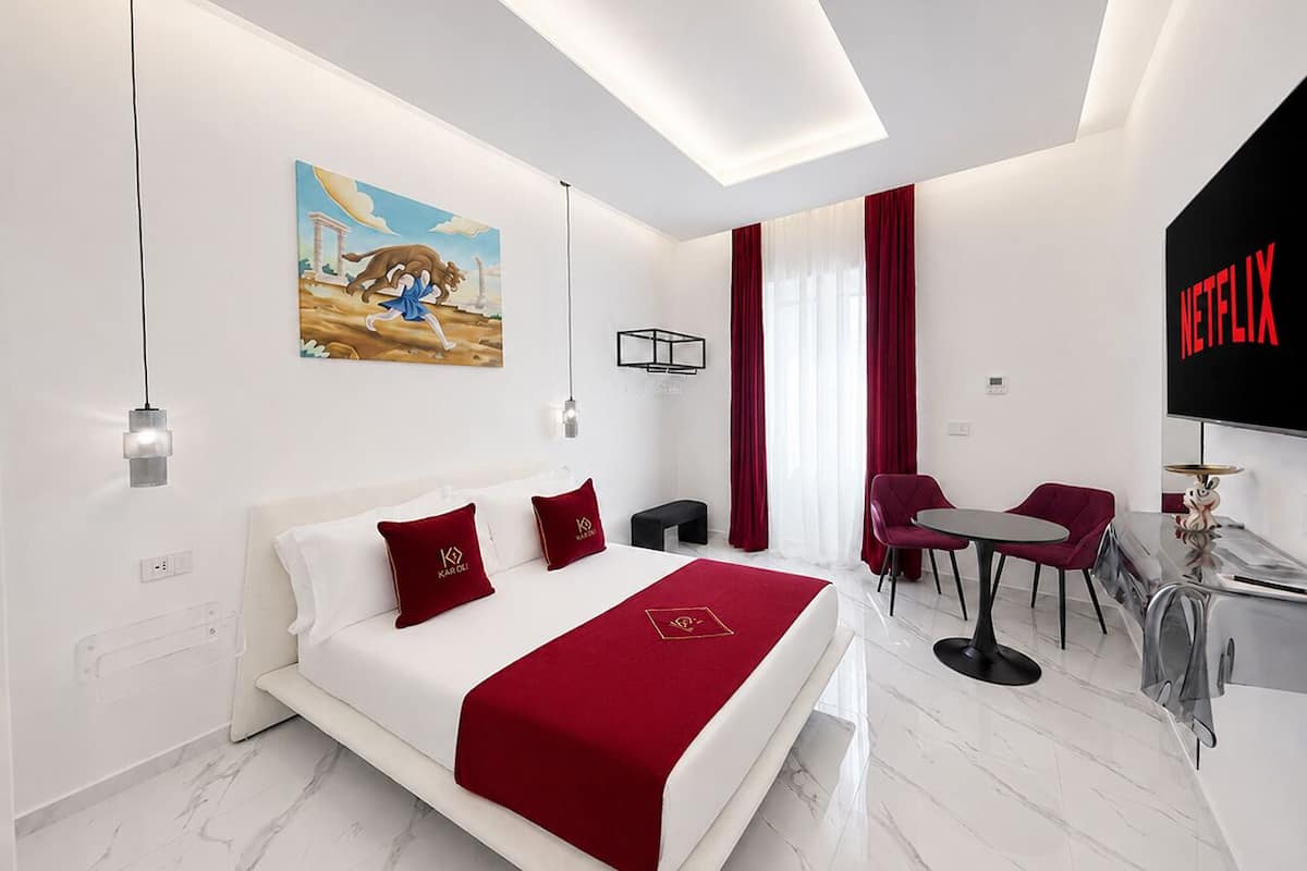 Quarto de hotel moderno com cama, escrivaninha, cadeira, televisão e um quadro na parede.
