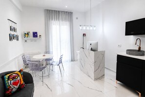 A modern kitchen with a marble countertop, a dining area with a round table and chairs, a black sofa with a colorful pillow, and a mounted TV. - Kreart Suite & Rooms (Crotone)