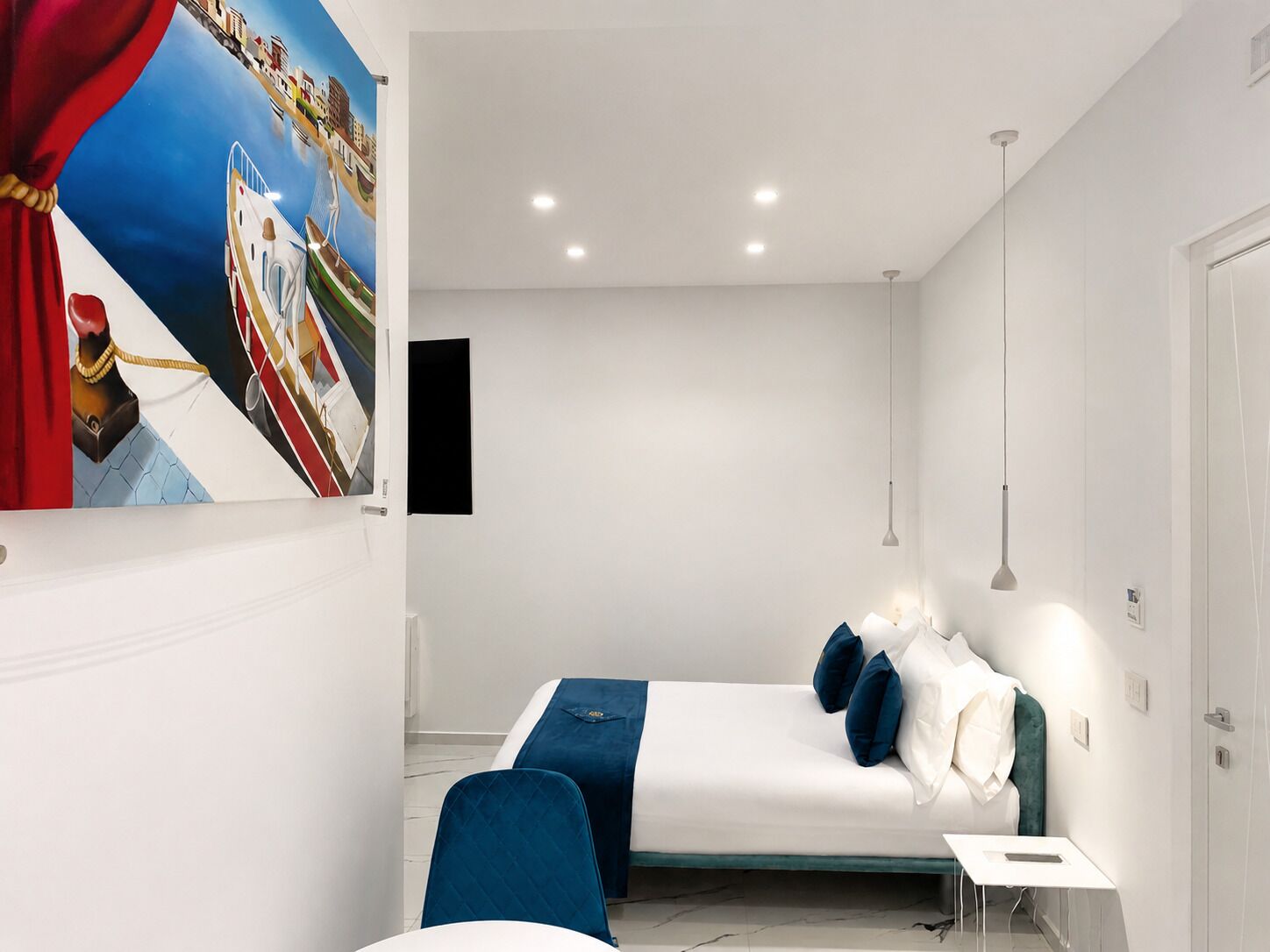 A modern bedroom with a bed, bedside tables, a chair, a painting, and a pendant light.