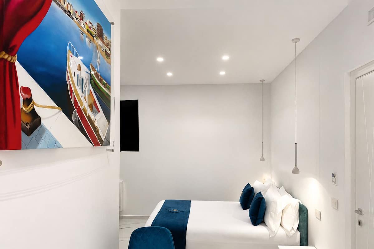A modern bedroom with a bed, bedside tables, a chair, a painting, and a pendant light.