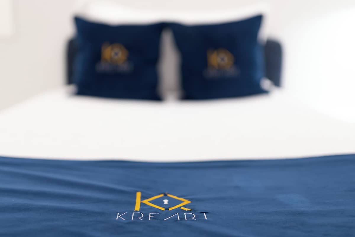 Cama com colcha e almofadas azuis com logotipo.