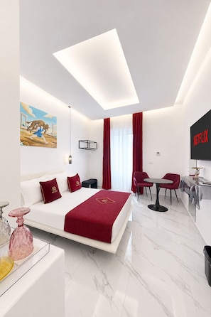 A modern hotel room with a bed, a desk, a chair, a TV, and a painting on the wall. - Kreart Suite & Rooms (Crotone)