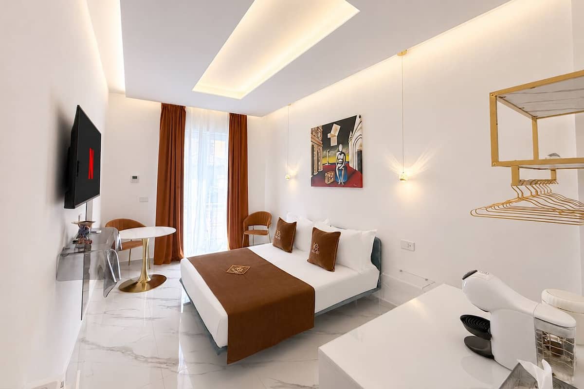 Quarto de hotel moderno com cama, escrivaninha, cadeira, televisão e um quadro na parede.