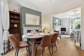 A dining area with a round table, four chairs, a bookshelf, a fireplace, and a television displaying 'NETFLIX'.