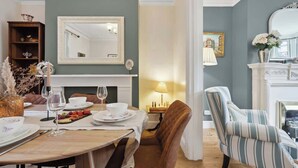 Un comedor con una mesa dispuesta para dos personas, chimenea, espejo y un sillón a rayas.