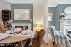 A dining area with a table set for two, a fireplace, a mirror, and a striped armchair.