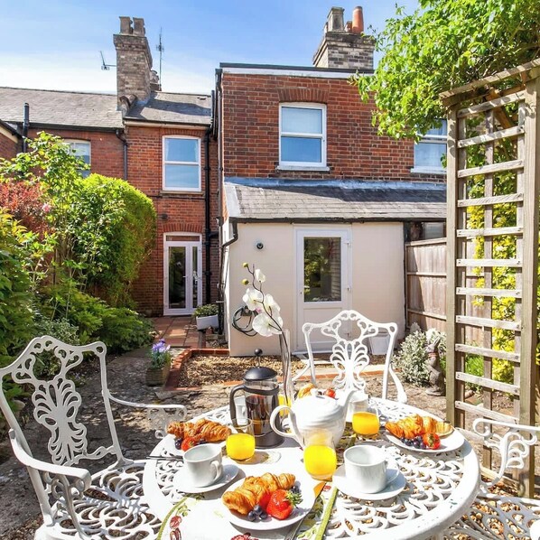 A patio with a table set for breakfast, surrounded by brick houses and greenery.