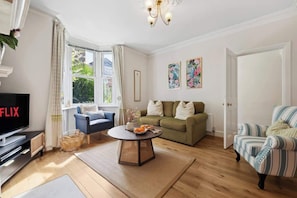 A living room with a TV, sofa, armchair, and a window with curtains.
