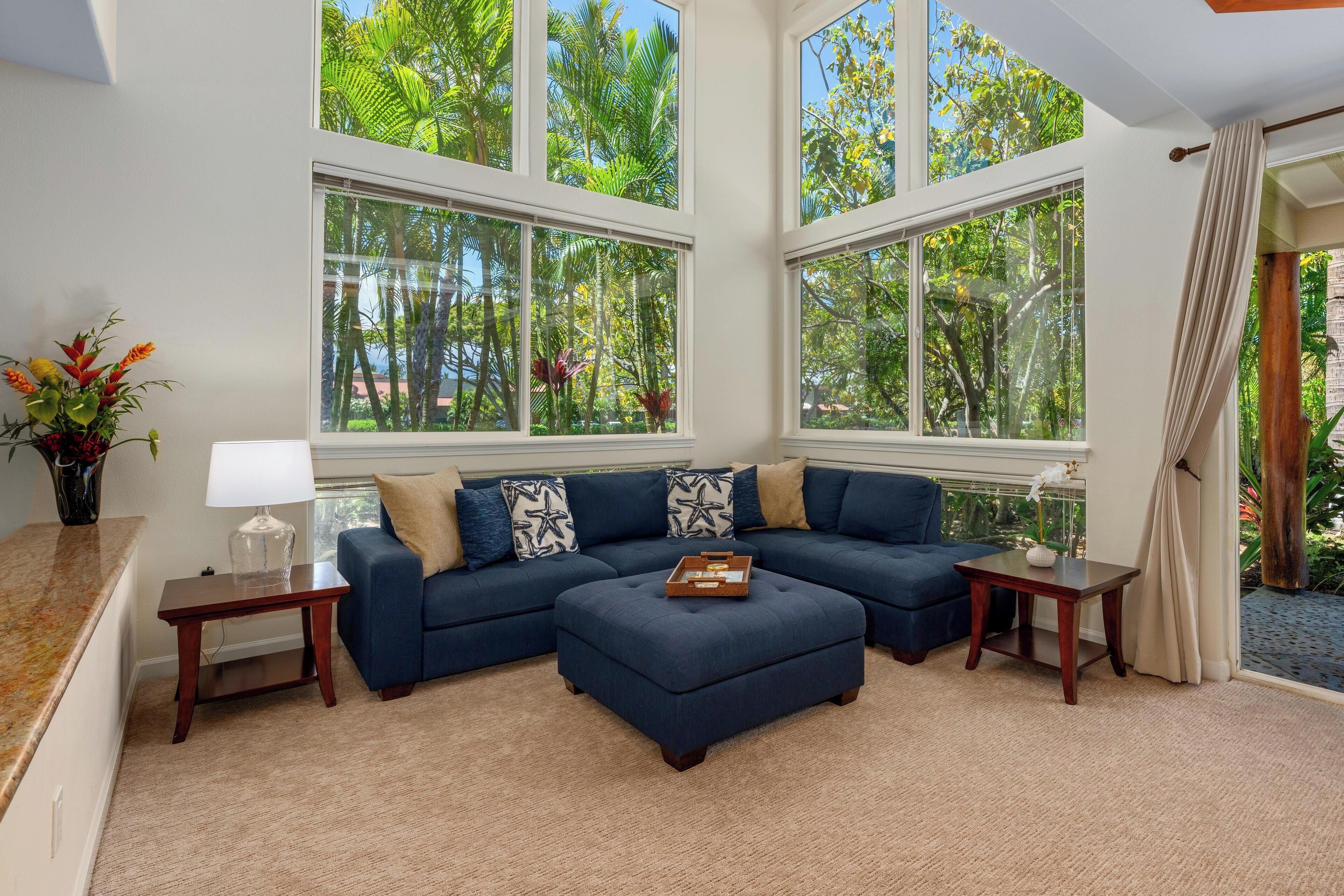 A living room with a sectional sofa, a coffee table, and large windows with a view of greenery.
